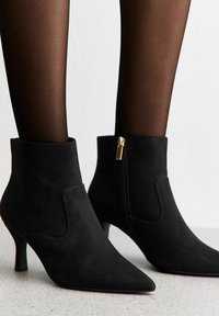 Stivaletti in suede neri con punta affilata e tacco basso. Presentano una zip laterale e una texture liscia.