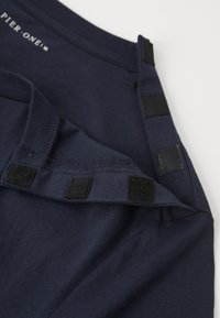 Tengerészkék pamut póló, kerek nyakkal és tépőzáras záródással a vállon. Simább textúrájú és megerősített varrású.