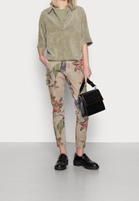 Olijfgroene gestructureerde blouse, beige cargobroek met bloemmotieven, zwarte gestructureerde handtas en zwarte platform instappers.