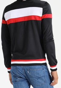 Sort jakke med lange ærmer, med horisontale røde og hvide striber hen over skuldrene og bundkanten, glat tekstur, sporty design.