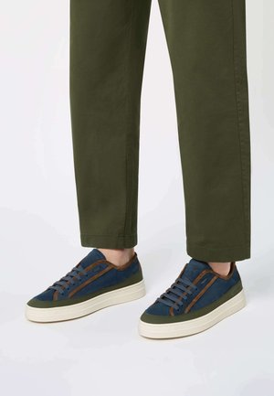Basketball avec un dessus bleu marine, des accents en suède marron et une semelle en caoutchouc crème. Les lacets correspondent à la tige ; un détail latéral texturé ajoute de la profondeur.