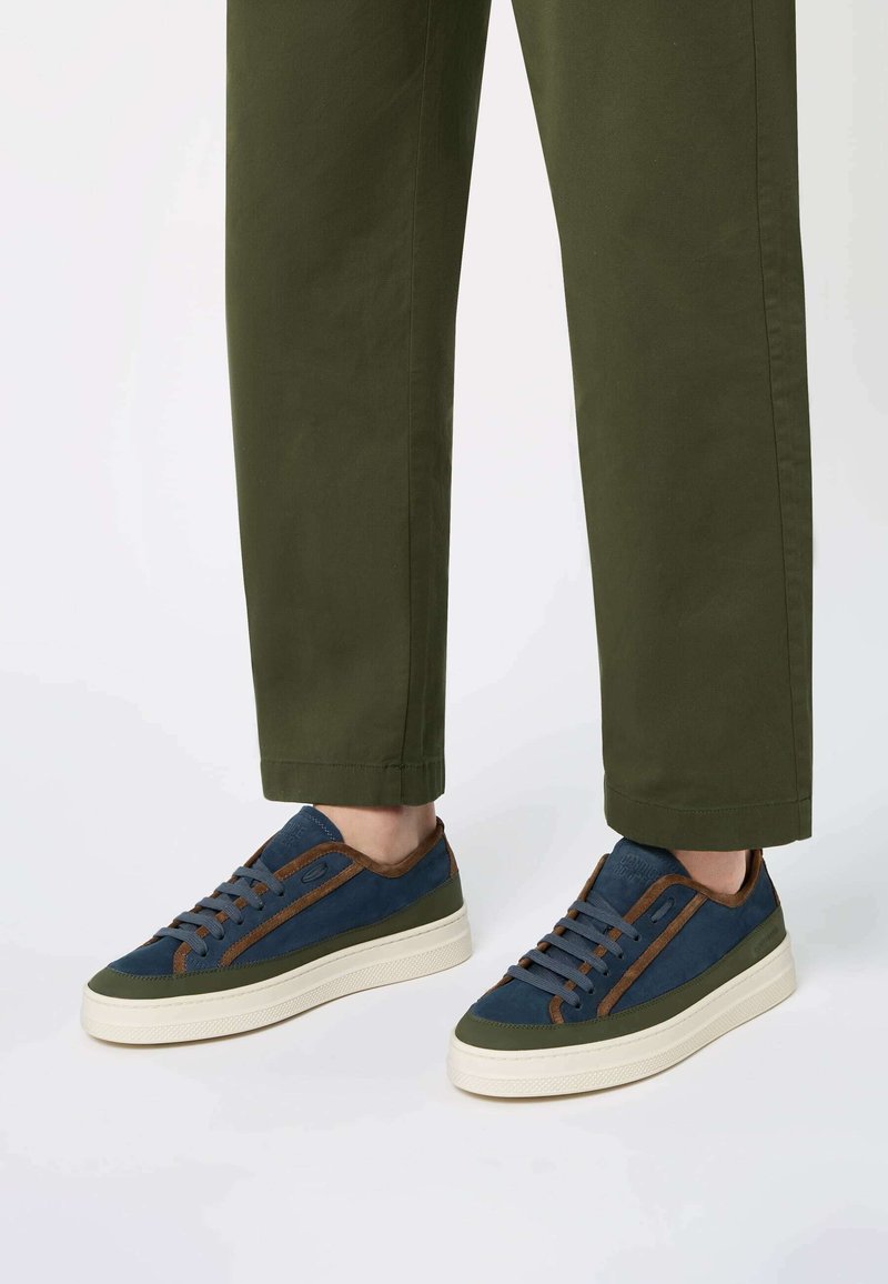 Basketball avec un dessus bleu marine, des accents en suède marron et une semelle en caoutchouc crème. Les lacets correspondent à la tige ; un détail latéral texturé ajoute de la profondeur.