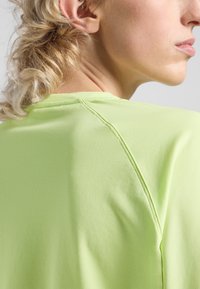 Top corto a maniche corte di un verde chiaro realizzato in un tessuto morbido e texturizzato. Presenta un collo arrotondato e cuciture visibili sulle spalle.