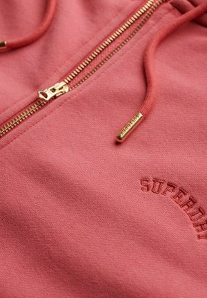 Roze ritsvoering hoodie met een gouden rits, zachte stoftextuur en 'SUPERDRY' subtiel geborduurd in een zachte tint aan de linkerkant.