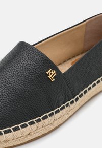 Zapato negro de cuero sin cordones con un acabado texturizado, que presenta una suela de yute trenzado y un acento de logo dorado en la parte superior.