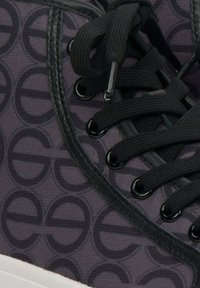 Zwarte sneaker met patroon, voorzien van een gemêleerde donkere stoffen bovenkant, zwarte veters, metalen oogjes en een witte rubberen zool.