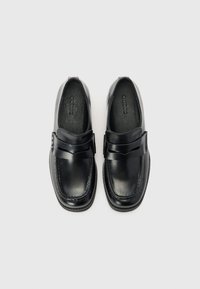 Chaussures en cuir noir avec une finition lisse, présentant un détail de sangle plate à l'avant-pied et un design à bout rond.