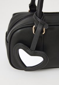 Sac à main noir en simili cuir avec fermeture éclair, présentant un accent en forme de cœur et une structure arrondie. Finition texturée.