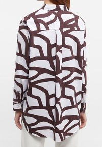 Camicia a maniche lunghe con un motivo astratto marrone e bianco, realizzata in tessuto morbido, con polsini abbottonati e piega sul retro per un tocco di dettaglio.