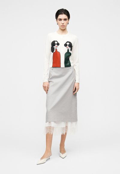 Jopica s tiskanim grafičnim vzorcem, ki prikazuje dve stilizirani ženski v rdeči in zeleni barvi, kombinirana s sivim svinčnikom krilo in belim čipkastim robom.