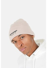 Berretto in maglia rosa con design a risvolto e la scritta "SIXTH JUNE PARIS" ricamata in nero, indossato da una persona con una felpa bianca.