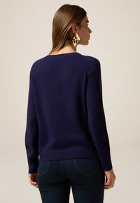 Granatowy sweter wykonany z miękkiego, teksturowanego materiału z długimi rękawami i okrągłym dekoltem. Posiada ściągacz na dolnym brzegu i prosty design.