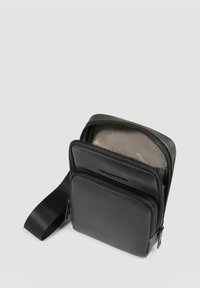 Schwarze Nylon-Umhängetasche mit zwei Reißverschlussfächern, verstellbarem Riemen und glatter, matter Oberfläche. Mit Logo auf der Vorderseite.