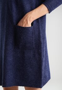 Mörkblå tröjklänning i mjukt, texturerat material, med en sidficka och långa ärmar. Enkelt, rakt snitt utan dekorationer.