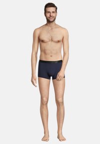 Navy blue boxer briefs with a black elastic waistband, smooth texture, fitted design, and short leg coverage, worn by a standing male model.