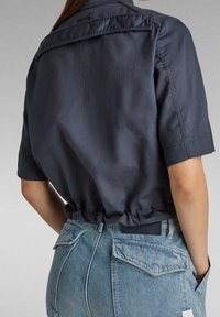 Mörkblå kortärmad skjorta med elastisk fåll, i kombination med ljusblå jeans i denim med bakfickor och en logotag på midjan.