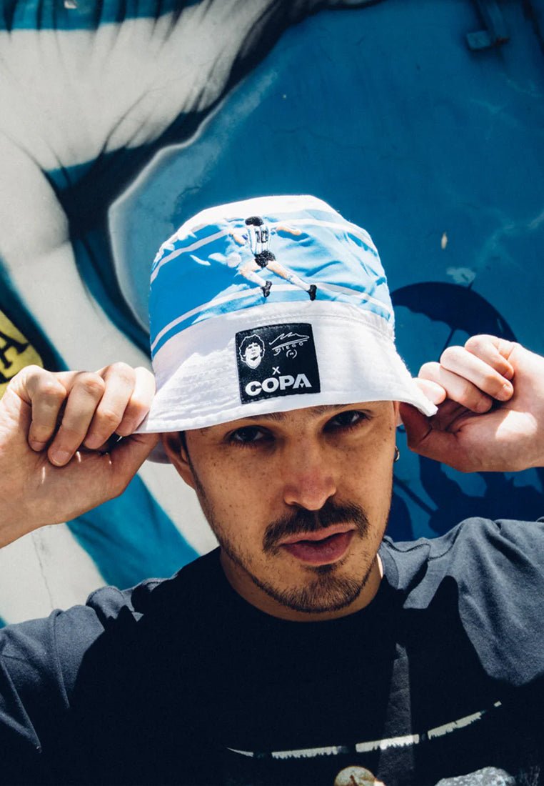 Blauwe bucket hat met een sportdesign featuring een speler, witte rand en een zwart logo label met "COPA." Gemaakt van katoen, casual fit.