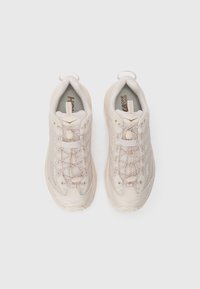 Une paire de baskets de sport beiges avec des panneaux en maille et des lacets élastiques sans nœud, vue de dessus sur un fond blanc.
