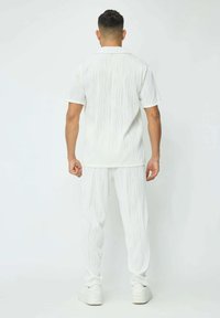 Ensemble léger en blanc comprenant une chemise et un pantalon avec des motifs de vagues, des manches courtes et une coupe décontractée, associé à des baskets blanches.