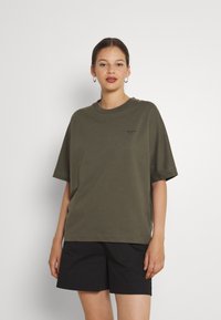 T-shirt oversize verde oliva in morbido cotone, maniche corte, scollo rotondo, con piccolo dettaglio del logo sul petto, abbinato a pantaloni corti neri.