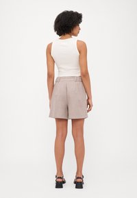 Un top alb fără mâneci asortat cu pantaloni scurți bej deschis, cu talie înaltă, care prezintă bucle pentru curea și un design ajustat, văzut din spate.