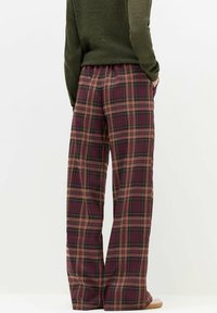 Ruudulliset housut, joissa on löyhä istuvuus, burgundin sävyissä ja vihreässä sekä beigeissä kuvioissa, joustava vyötärö ja kevyttä kangasta.