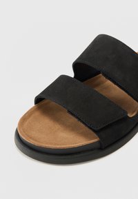 Black suede sandal with two wide adjustable straps, tan soft interior, and a black rubber sole. Simple design with no additional patterns.