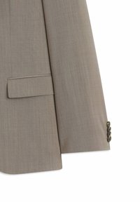 Manche d'une veste de costume beige avec quatre boutons et une poche à rabat sur un fond blanc uni.