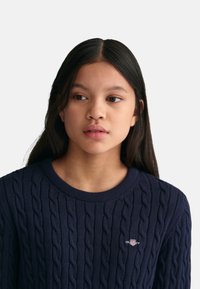 Maglione lavorato a maglia blu navy con un motivo a trecce testurizzato, scollo rotondo a coste e un piccolo logo ricamato sul petto.