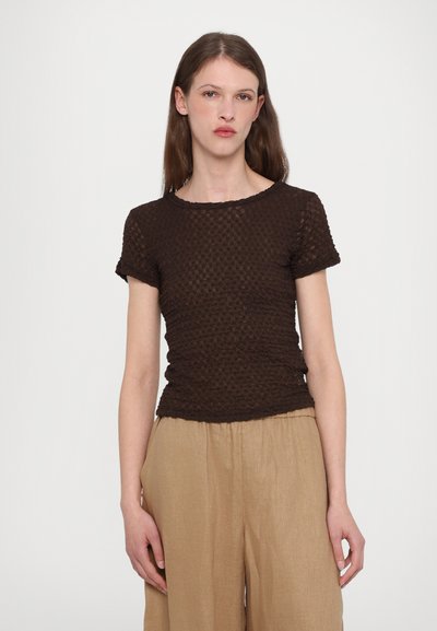 Brązowa bluzka krótki rękaw o teksturowanej powierzchni, z okrągłym dekoltem i dopasowanym krojem, zestawiona z luźnymi beżowymi spodniami z lnu.