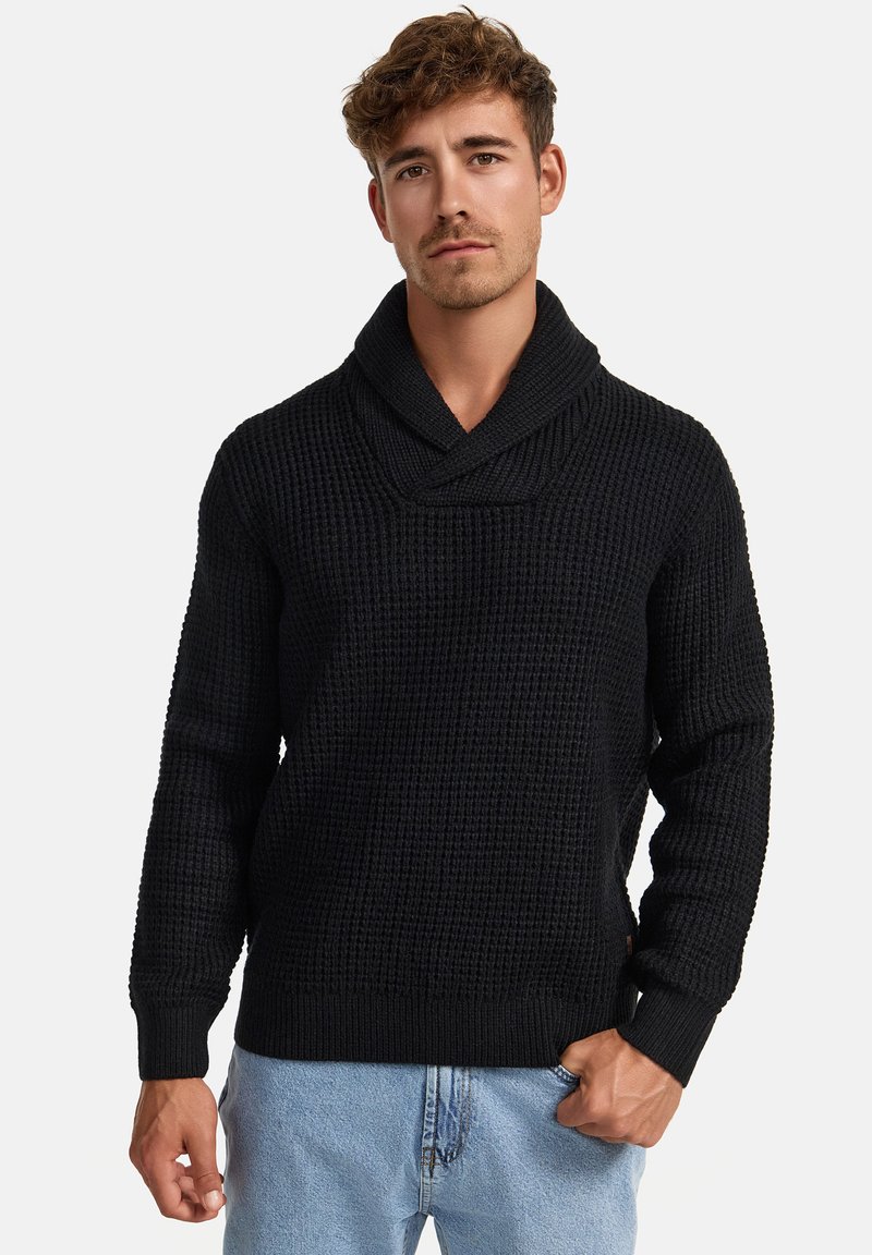 Svart genser med teksturert strikkemønster, sjalkrage, lange ermer og ribbestrikkede mansjetter og nederkant. Kombinert med lyseblå jeans.