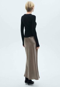 Zwarte lange mouw top en een lange, gladde, taupe rok met een subtiele glans, gedragen met zwarte schoenen. Minimalistisch ontwerp, aansluitende silhouet.