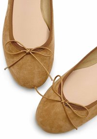Ballerines en suède marron avec un bout arrondi, ornées d'un nœud à l'avant et d'un bord contrastant marron le long de l'ouverture. Doublure intérieure lisse.