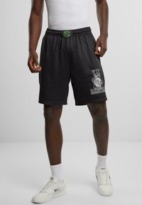 Pantaloni corti da basket neri in tessuto a rete, con cintura elastica e dettagli verdi, caratterizzati da una stampa grafica sulla gamba sinistra.