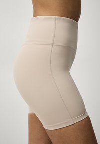 Beige højtaljede shorts lavet af glat, strækbart materiale. Har syede sømme og en tætsiddende design for komfort.