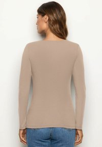 Hihaton beige paita ribbaatukaisesta materiaalista, jossa on pyöreä kaula-aukko ja slim fit -malli, yhdistettynä sinisiin farkkuihin.