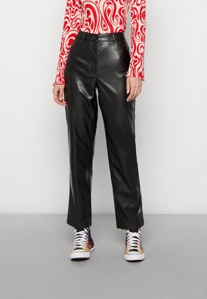 Woman wearing black high-waist faux leather pants, a long-sleeve red and white patterned top, and multicolored high-top sneakers.