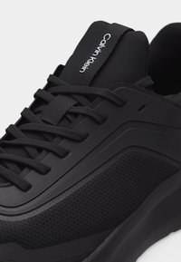 Μαύρο αθλητικό παπούτσι Calvin Klein με πλευρές από υφασμάτινο πλέγμα με υφή, λείες επικαλύψεις και λουράκι με το λογότυπο στη γλώσσα, δεμένα κορδόνια.