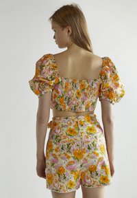 Top corto floreale con maniche a sbuffo nelle tonalità di arancione e rosa. Pantaloni corti a vita alta coordinati con un vivace motivo floreale e una cintura annodata.