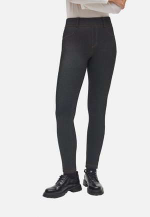 Leggings gris oscuro con una textura similar al denim, con detalles de costura en naranja y una cintura alta, combinados con zapatos negros de suela gruesa.