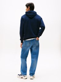 Felpa navy con cappuccio regolabile, abbinata a jeans azzurri a gamba larga. Sneakers bianche e navy completano l'outfit casual.