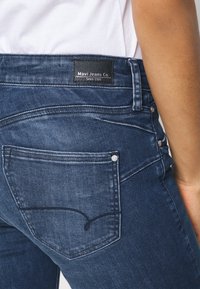 Tummat farkut, joissa on kapea malli. Ominaisuuksina erottuva takataskun ompelukuviot ja Mavi Jeans Co. -merkki vyötäröllä.