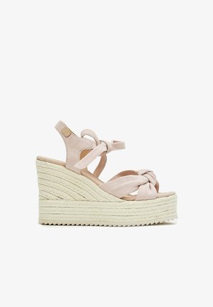 Sandalia de cuña beige con suela de cuerda trenzada, tiras delanteras anudadas y lazo en el tobillo sobre fondo blanco.