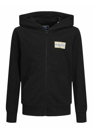 Haut de sweat à zip noir avec poches avant et patch logo, pantalon cargo beige avec poches latérales, et baskets noires avec rayures blanches.