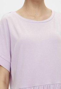 Jasnofioletowa bluzka z krótkim rękawem o okrągłym dekolcie i zgromadzonym wykończeniu. Wykonana z miękkiego materiału o gładkiej fakturze.