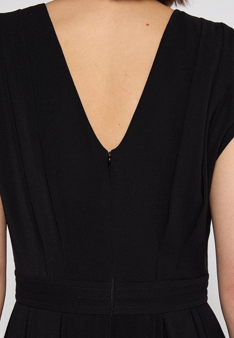 Schwarzes Kleid mit tiefem V-Ausschnitt, kurzen Ärmeln und tailliertem Bund. Strukturierter Stoff mit einem Reißverschluss auf der Rückseite.