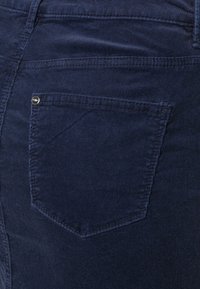 Tissu en velours côtelé bleu marine avec une surface texturée, comportant une seule poche arrière avec un accent de rivet en métal. Aucune autre décoration visible.