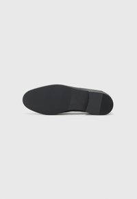 Black leather shoe sole with a smooth matte finish, slightly rounded shape, and textured rubber traction pattern for grip.