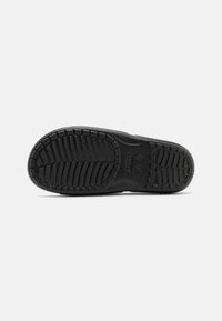 Suela de zapatilla negra con goma texturizada para mayor agarre, con patrones de tracción distintivos y bordes curvados. Logo prominente visible.