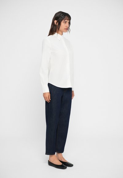 Camicia bianca a maniche lunghe con colletto, abbinata a jeans larghi blu scuro e scarpe nere piatte. Design semplice e pulito.
